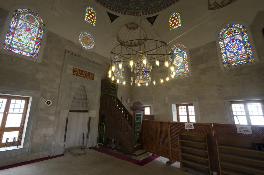 Şemsi Paşa Camii'nin içi; ortada halkalı avize, mermer mihrap, ahşap minber, renkli camlı pencereler.