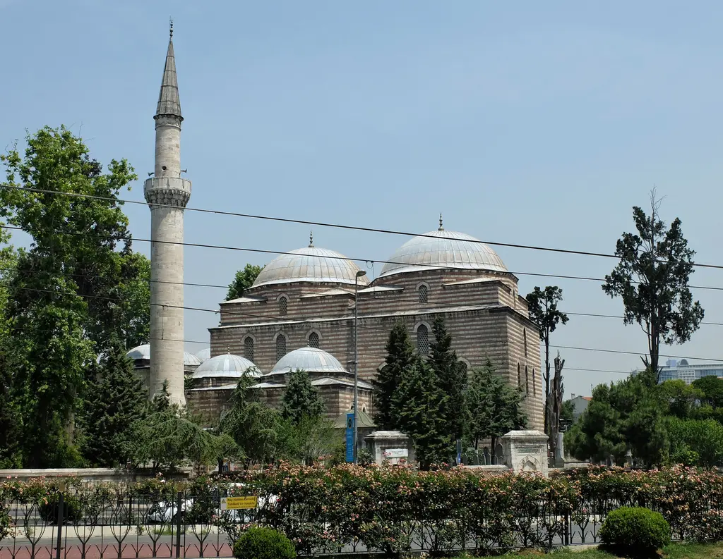 Aksaray'da Murat Paşa Camii; kurşun kaplı kubbeler, kemerli son cemaat yeri, yanında yüksek minare, avludaki ağaçlar ve önde taş duvar.