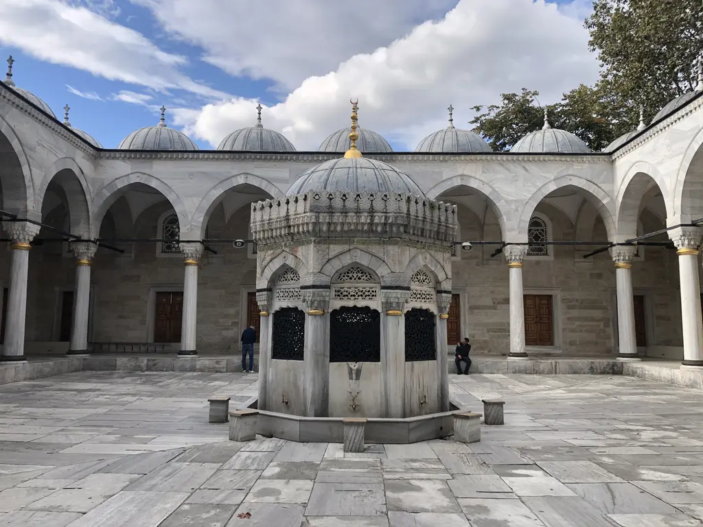 Yeni Valide Camii'nin avlusu; ortada kubbeli mermer şadırvan, çevresinde kemerli revaklar ve küçük kubbeler.