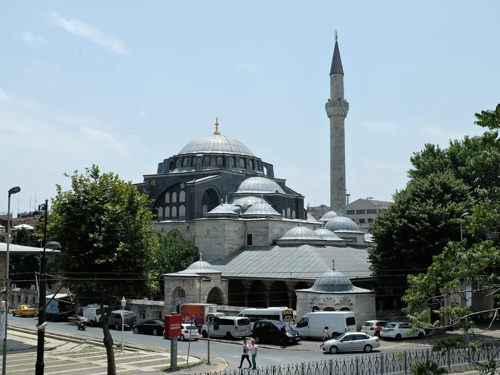Tophane'de caddeden Kılıç Ali Paşa Camii; ağaçların ardında kubbeler ve minare, önde son cemaat yerinin kurşun çatısı ve park etmiş araçlar.