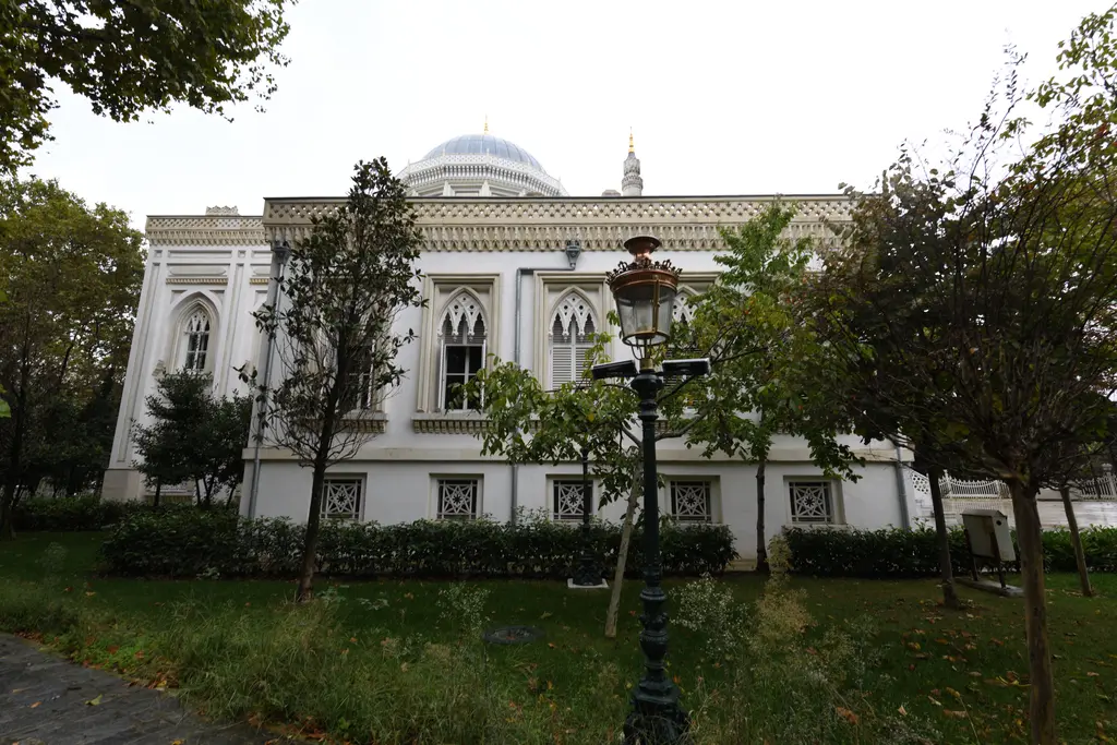 Yıldız Hamidiye Camii'nin güneydoğu cephesi; sıra sıra sivri kemerli pencereler, çim alan, ağaçlar ve fener direği.