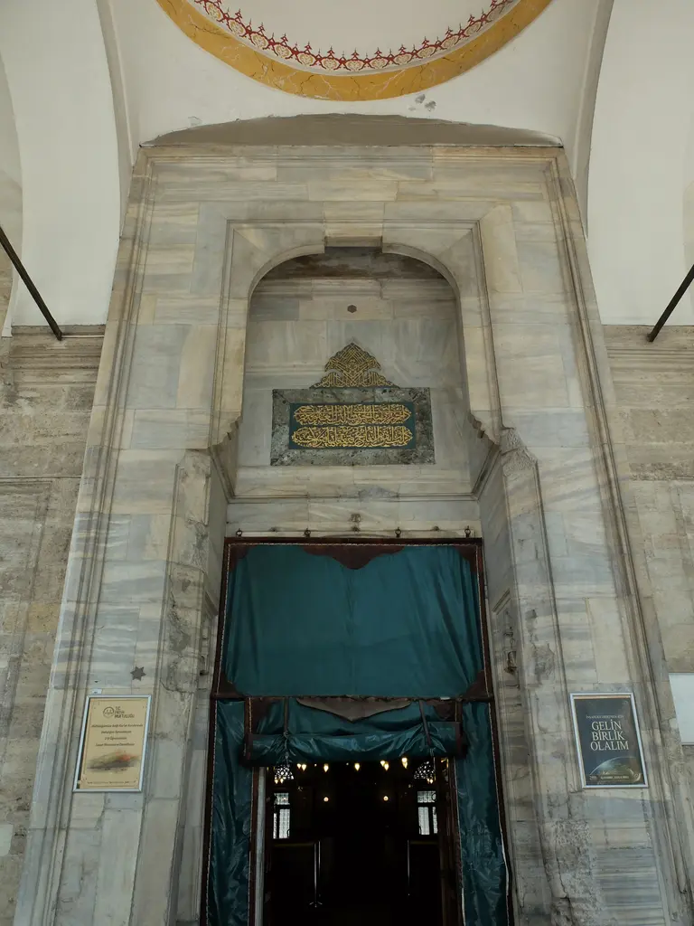 Murat Paşa Camii'nin cümle kapısı; mermer çerçeve, niş içinde altın yazılı kitabe, üstünde palmet biçimli yazı ve yeşil kapı perdesi.