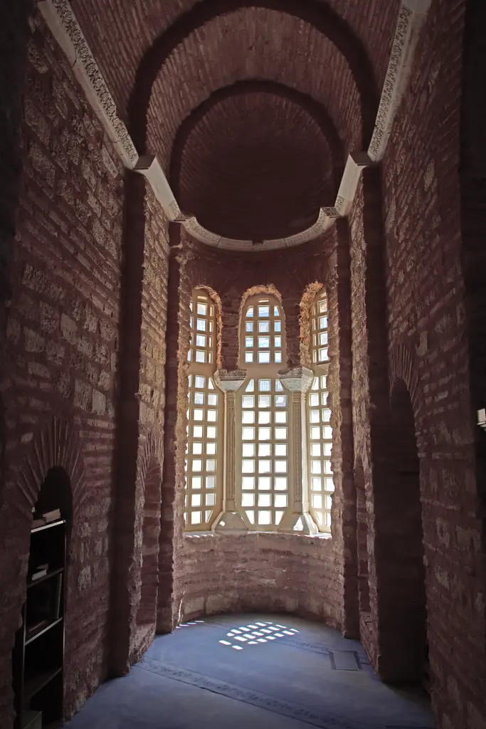 Fenari İsa Camii'nde yan şapel; tuğla örgülü dar apsis, ortada uzun mermer şebekeli pencereler, kemerli yarım kubbe ve zeminde pencerelerden düşen ışık deseni.