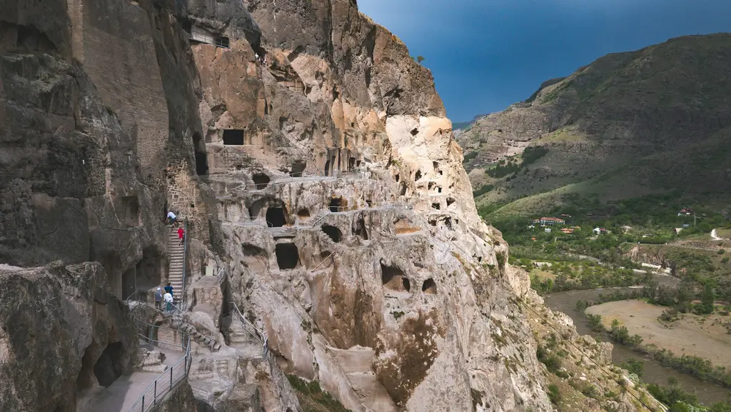 Vardzia'da dik bir kaya yüzüne oyulmuş çok katlı mağara manastırı; sıra sıra oyuk pencereler ve aşağıda yeşil vadi.