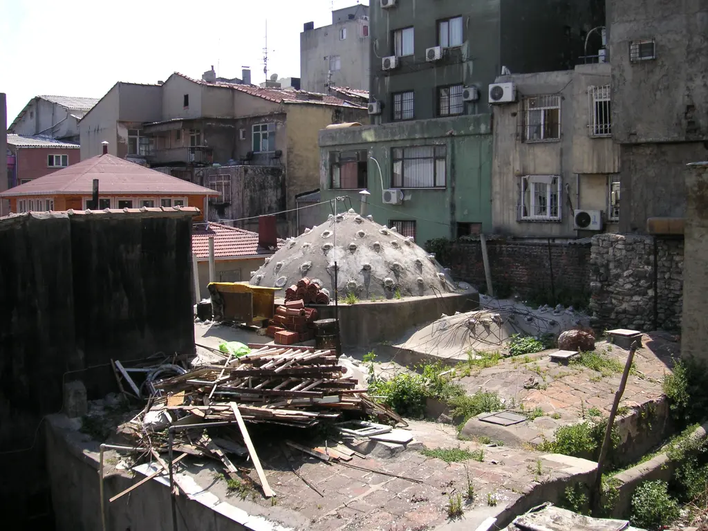 Ayakapı Hamamı'nın kubbelerine yukarıdan bakış; delikli kubbeler, çevrede moloz ve odunlar, arkada apartmanlar.
