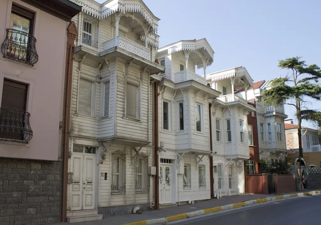 Kuzguncuk'ta sokak boyunca dizilen evler; beyaz ahşap cepheler, çıkmalar, demir parmaklıklı pencereler ve ağaçlar.