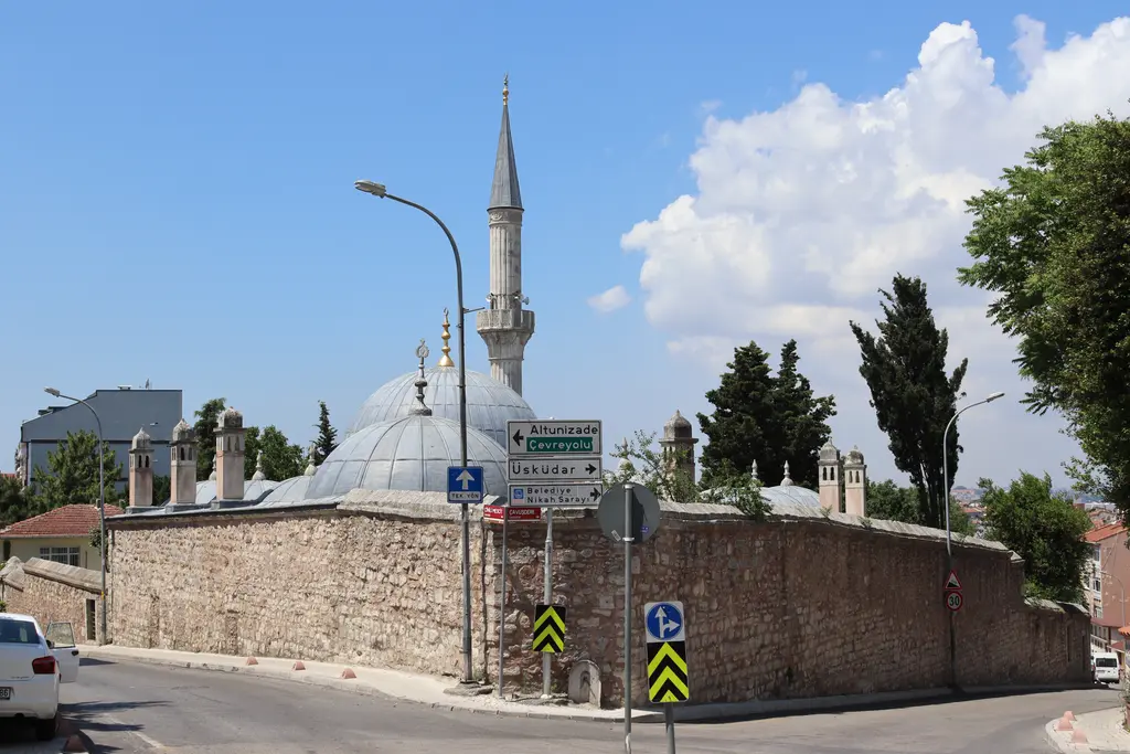 Çinili Camii çevresinde köşe; tuğla ve taş örgülü avlu duvarı, arkada kubbeler, minare ve trafik levhaları.