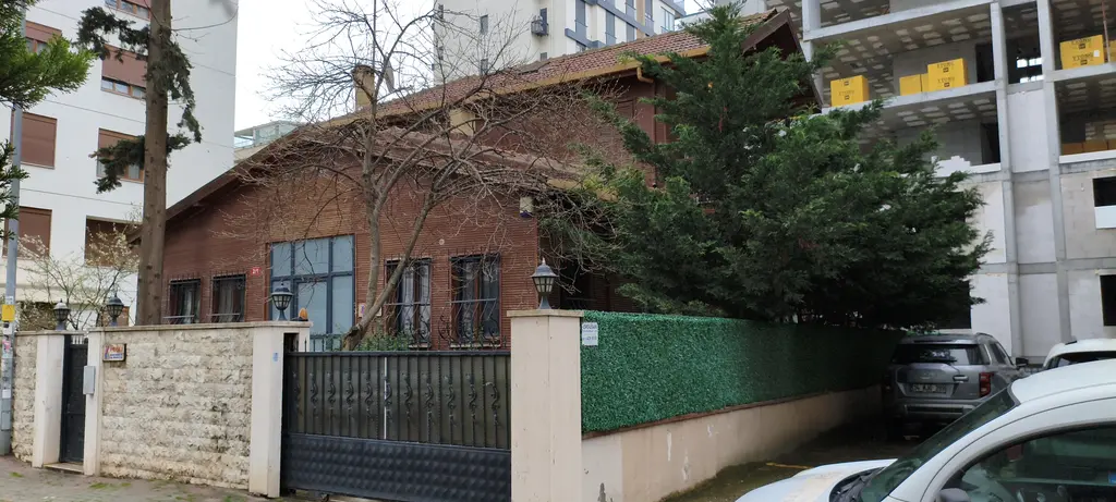 Göztepe'de Bestekâr Ziya Sokağı'nda konak; tek katlı kahverengi ahşap yapı, taş duvar, demir kapı ve yanında inşaat.