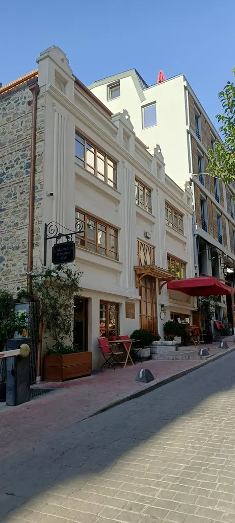 Çukurcuma Caddesi'nde tarihi hamam binası boyunca uzanan sokak; taş cepheler, dükkânlar ve mavi gökyüzü.