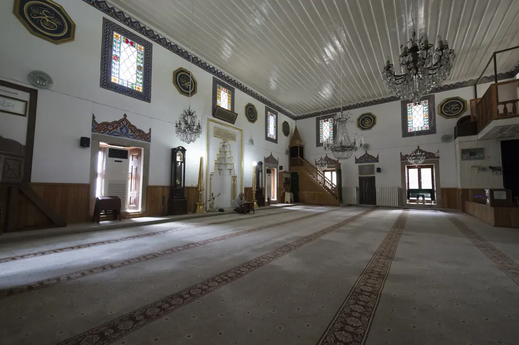 İskender Paşa Camii'nin içi; ahşap tavan, avize, kadınlar mahfili, renkli camlı pencereler ve halı kaplı zemin.