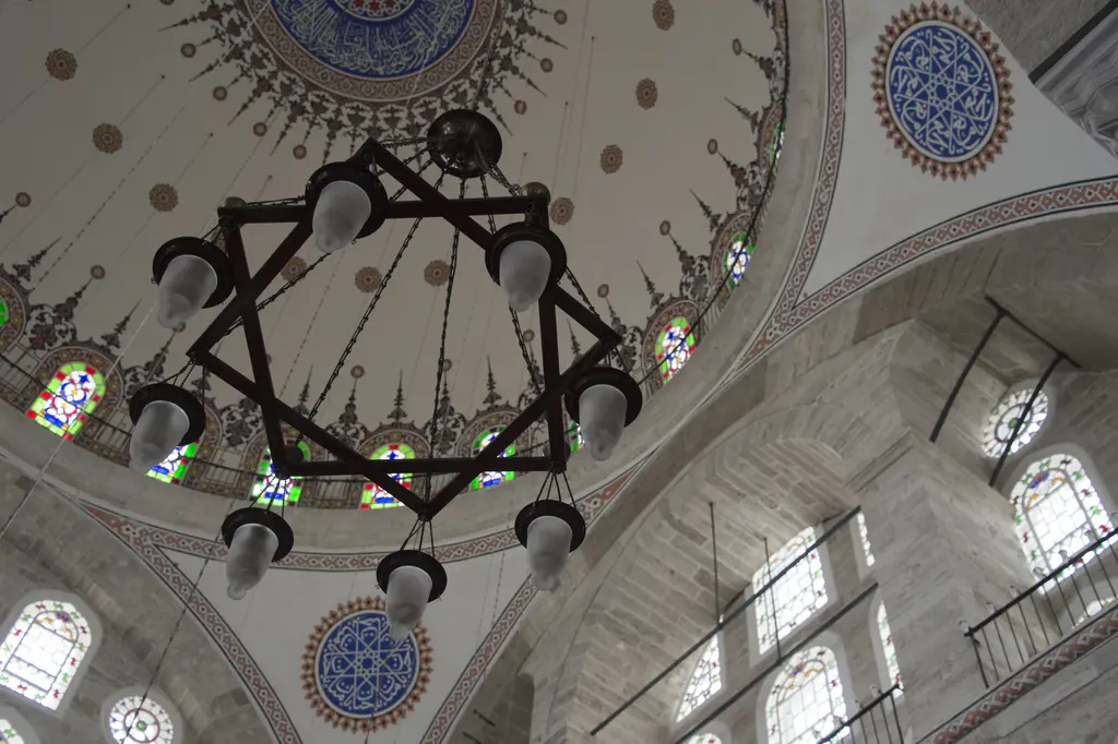 Mihrimah Sultan Camii'nin kubbesi içeriden; kubbe göbeğindeki yazı madalyonu, çevresindeki kalem işi bezemeler, pandantifler ve avize zinciri.