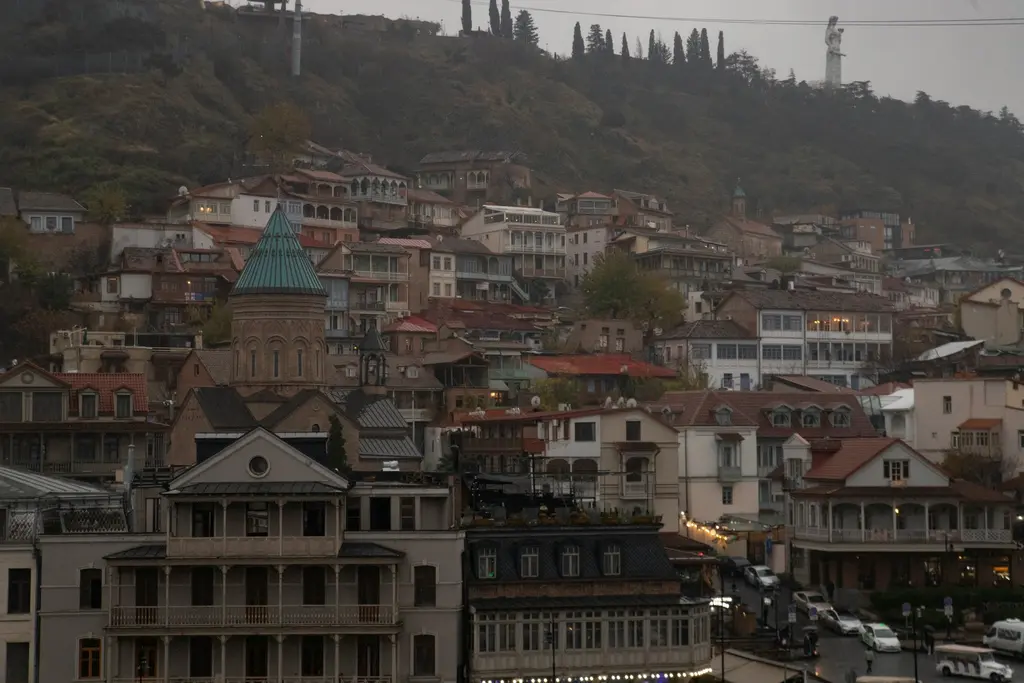 Tiflis'te Narikala Kalesi'nden eski şehir; tepedeki taş surlar, aşağıda kırmızı çatılı evler ve nehir kıyısındaki kubbeli yapılar.