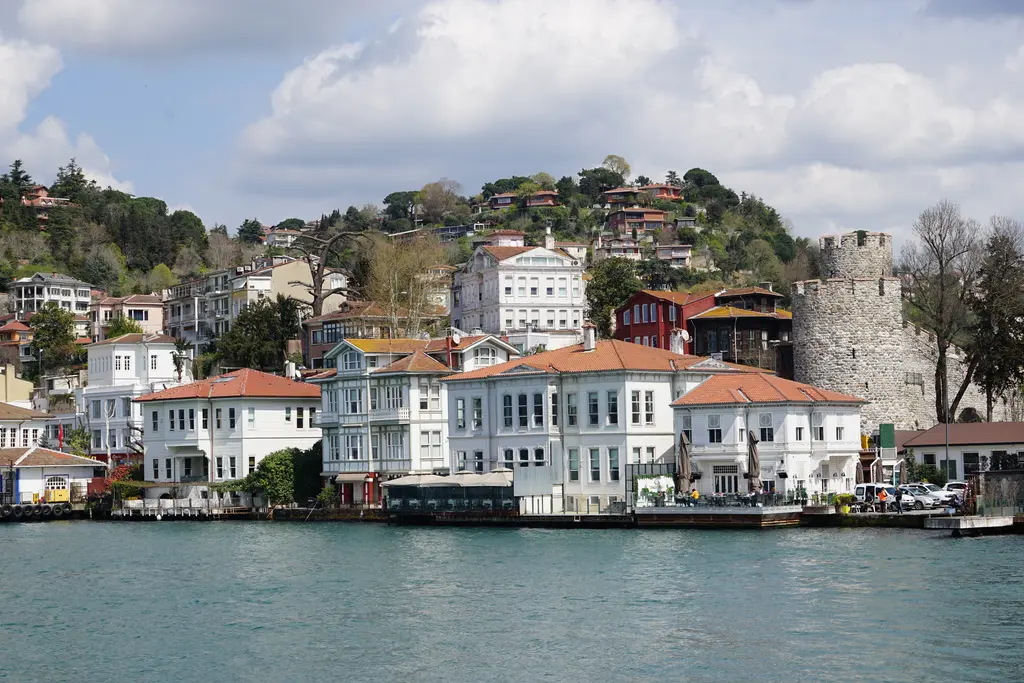 Anadoluhisarı'nda yalılar; Boğaz kıyısında dizilen beyaz ve kırmızı yalılar, sağda hisarın yuvarlak kulesi ve yamaçta evler.