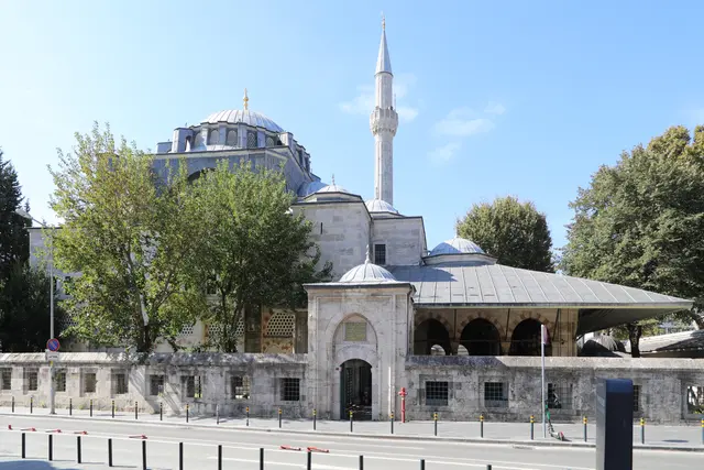 Tophane'de Kılıç Ali Paşa Camii; kurşun kaplı kubbeler, tek şerefeli ince minare, önde meyilli çatılı son cemaat yeri, taş avlu duvarı ve ağaçlar.