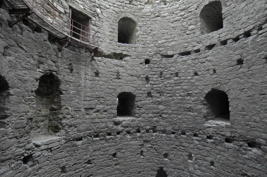 Yuvarlak bir kulenin içinden yukarı bakış; dairesel taş duvarda iki sıra kemerli mazgal nişi, duvarda sıra sıra hatıl yuvaları ve sol üstte modern demir korkuluklu servis platformu.