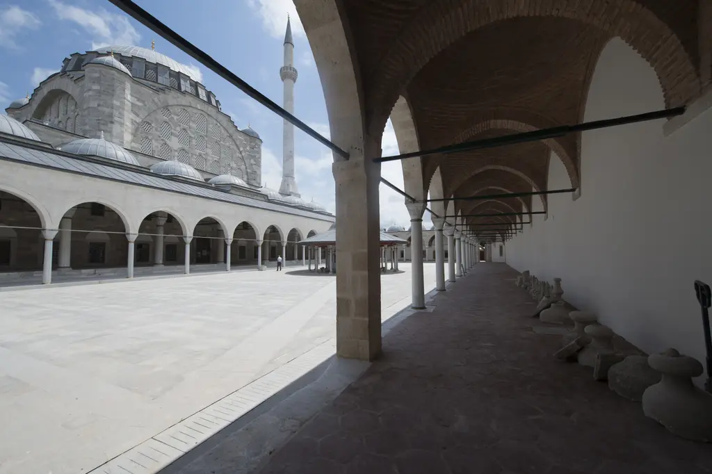 Mihrimah Sultan Camii avlusunda revak boyunca bakış; sütun ve sivri kemer dizisi, kırmızı boyalı ahşap tavan ve taş döşeli zemin.