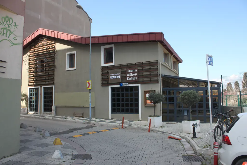 Kadıköy'de Tasarım Atölyesi; ahşap kaplamalı iki katlı bina, cam bölmeli giriş ve önünde parke taşlı sokak.