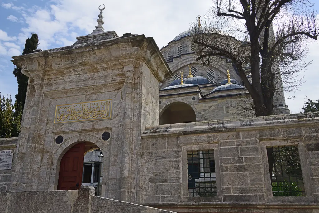 Ayazma Camii'nin avlu duvarı ve kapısı; kesme taş duvar, demir parmaklıklı pencereler ve arkada kubbe.