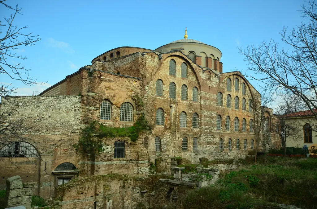 Kilise aşağıdan; taş temel duvarı, üstünde tuğla örgülü gövde, kemerli pencereler ve mavi gökyüzünde iki kademeli kubbe örtüsü.