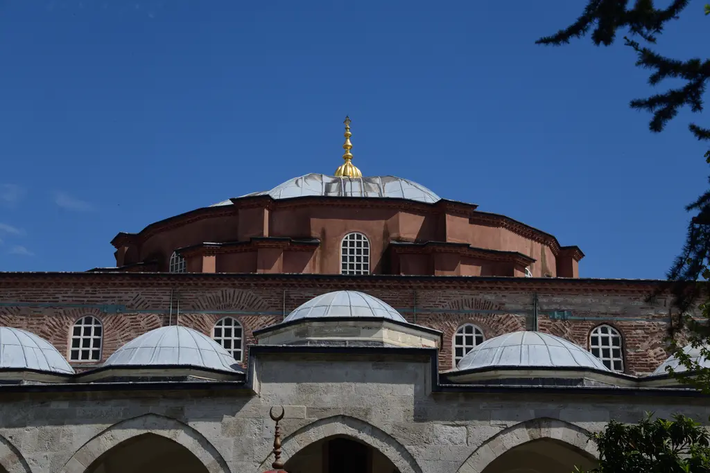 Küçük Ayasofya Camii'nin kubbesine avludan bakış; pembe kırmızı kasnak ve kemerli pencereler, gümüş rengi kurşun kubbe ile altın alem, altta son cemaat yerinin küçük kubbeleri.