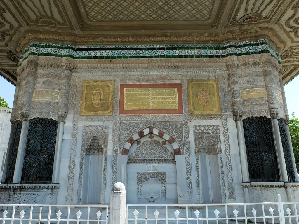 Çeşmenin güneybatı cephesi; ortada çeşme nişi, iki yanda tunç şebekeli sebil pencereleri ve üstte işlemeli saçak.
