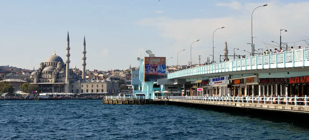 Galata Köprüsü'nün Eminönü ucu; köprünün beyaz korkuluklu gövdesi, sağda reklam panosu ve arkada Yeni Cami.
