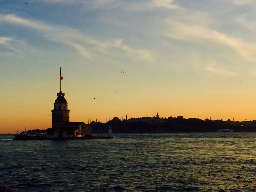 Gün batımında Kız Kulesi; turuncu gökyüzü önünde kulenin karanlık silueti, arkada tarihi yarımada.