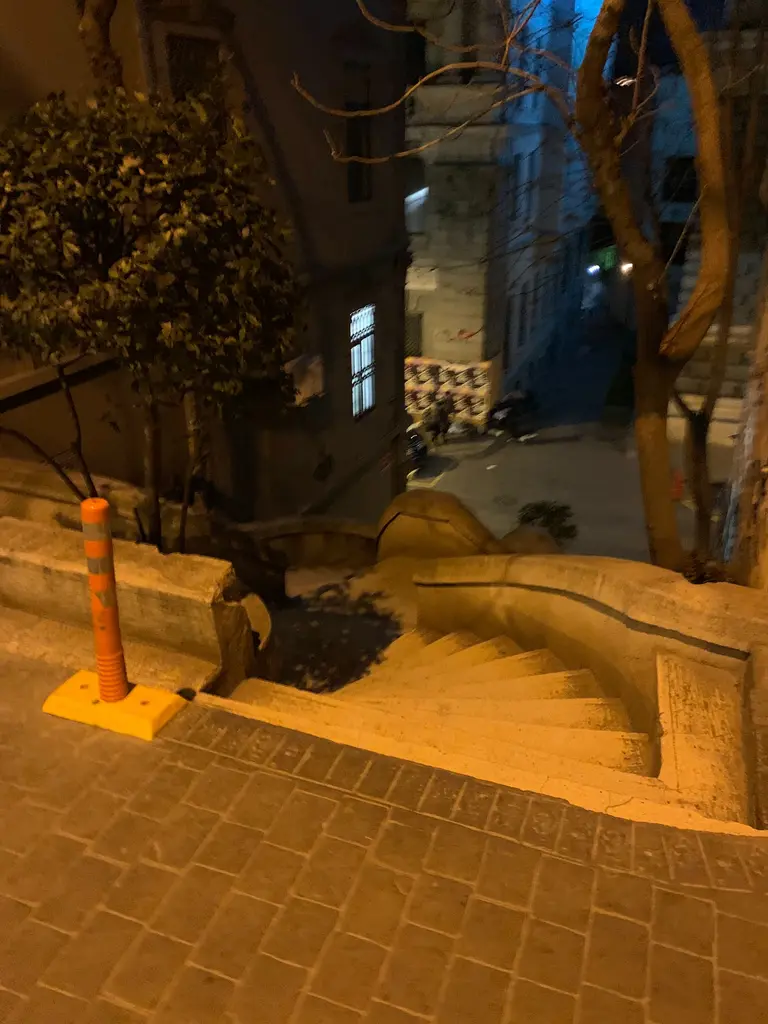 Gece Kamondo Merdivenleri; sokak lambalarının turuncu ışığı, karanlıkta seçilen basamaklar ve kenarda bir ağaç.