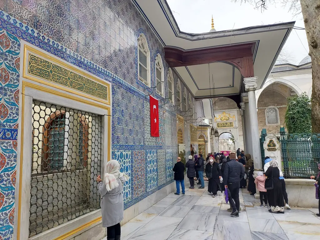 Eyüp Sultan Türbesi'nin duvarında çiniler; mavi, kırmızı ve yeşil çiçek desenli paneller ve "Muhammed" yazılı madalyon.