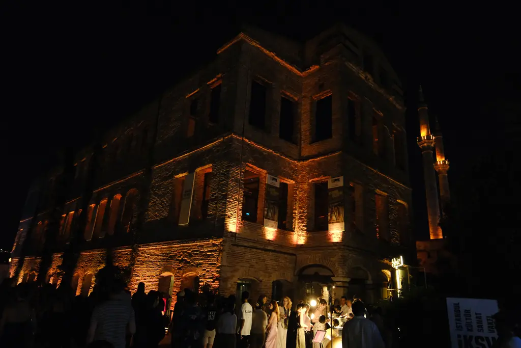 Gece Esma Sultan Yalısı'nın köşesi; sıcak ışıklı pencere boşlukları, karanlık gökyüzü ve önde insan siluetleri.