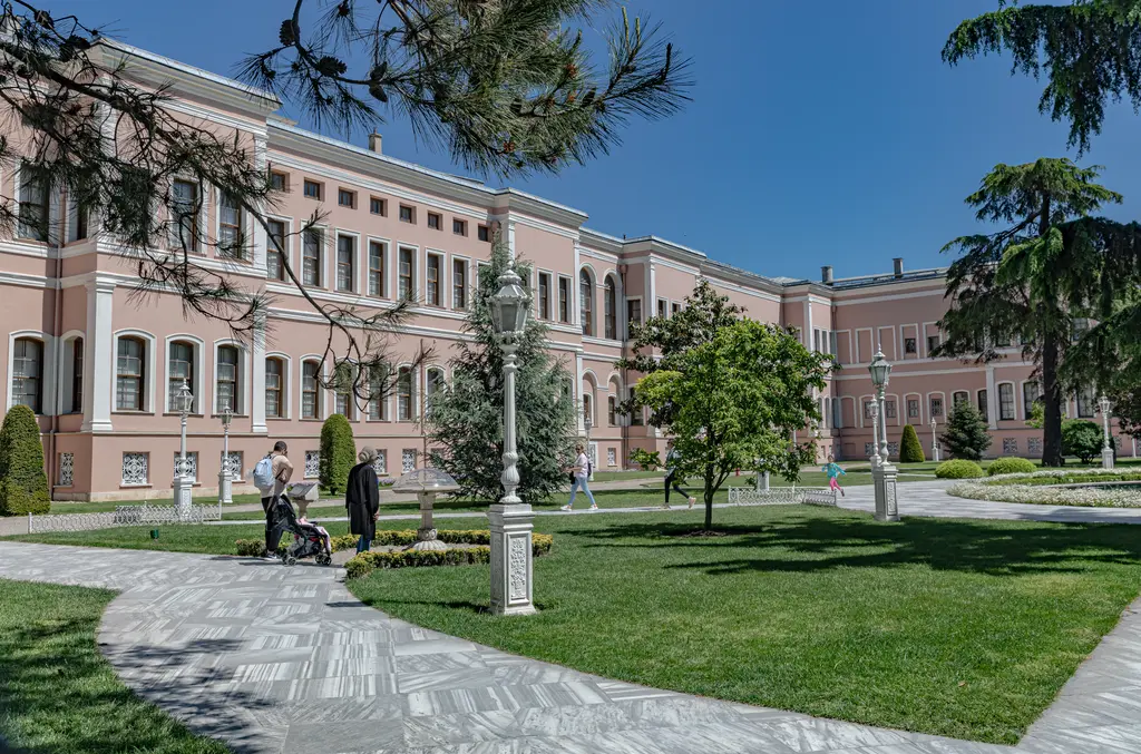 Dolmabahçe Sarayı'nın Harem bölümü; pembe cepheli uzun bina, sıra sıra pencereler, önde çimenler, ağaçlar ve yürüyüş yolu.