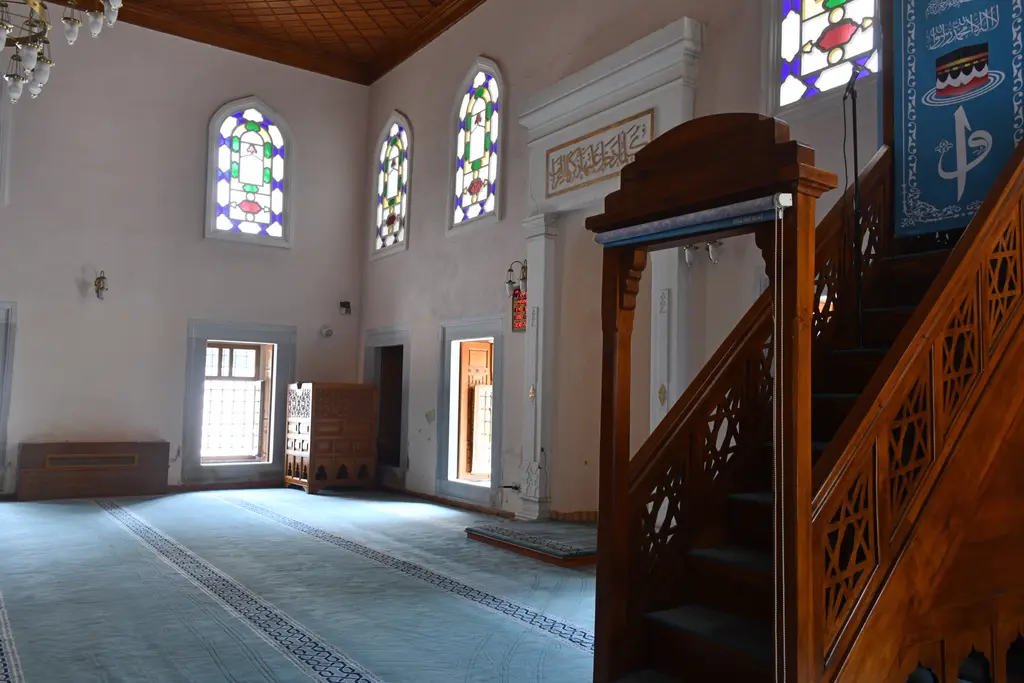 Şah Sultan Camii'nin minberi; ahşap korkuluklu merdiven, mavi örtülü külah, mihrap ve renkli camlı pencereler.