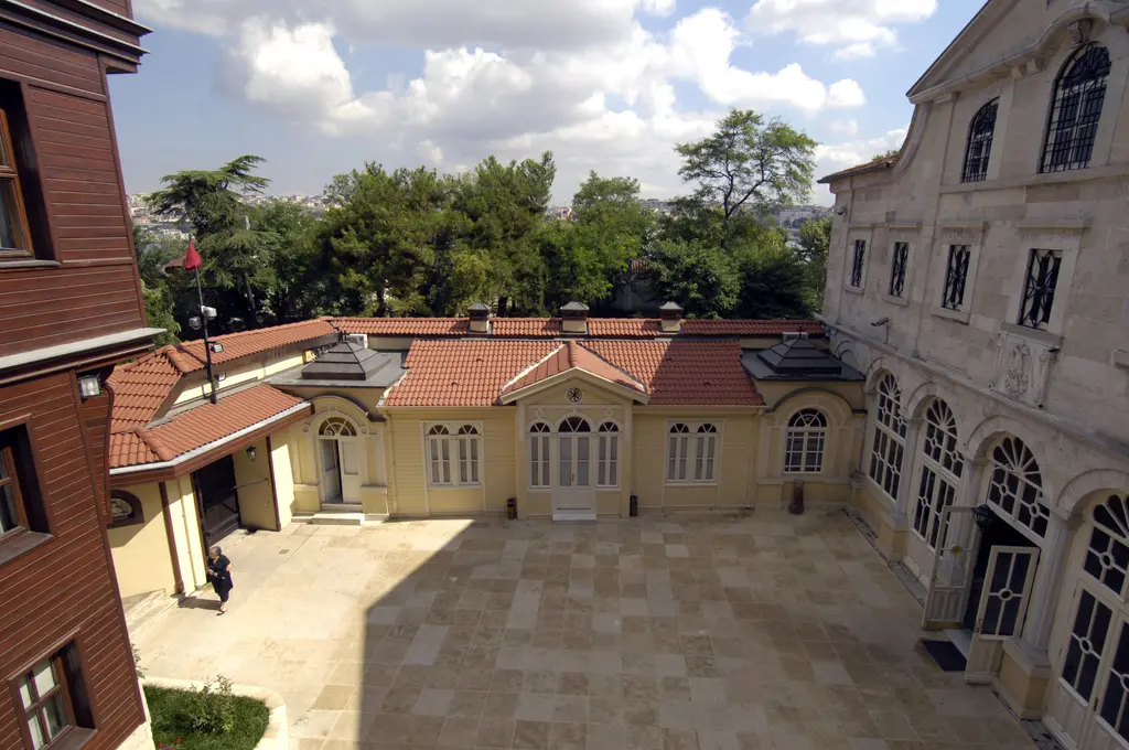 Fener Rum Patrikhanesi'nin avlusu; taş döşeli geniş avlu, kiremit çatılı sarı yapı, sağda kilise cephesi ve ağaçlar.