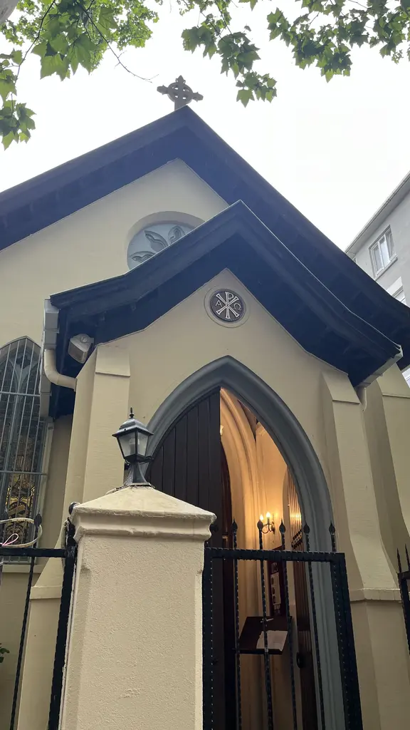 All Saints Moda Kilisesi'nin girişi; sivri kemerli kapı, haçlı alınlık, sarı duvar ve demir parmaklıklar.