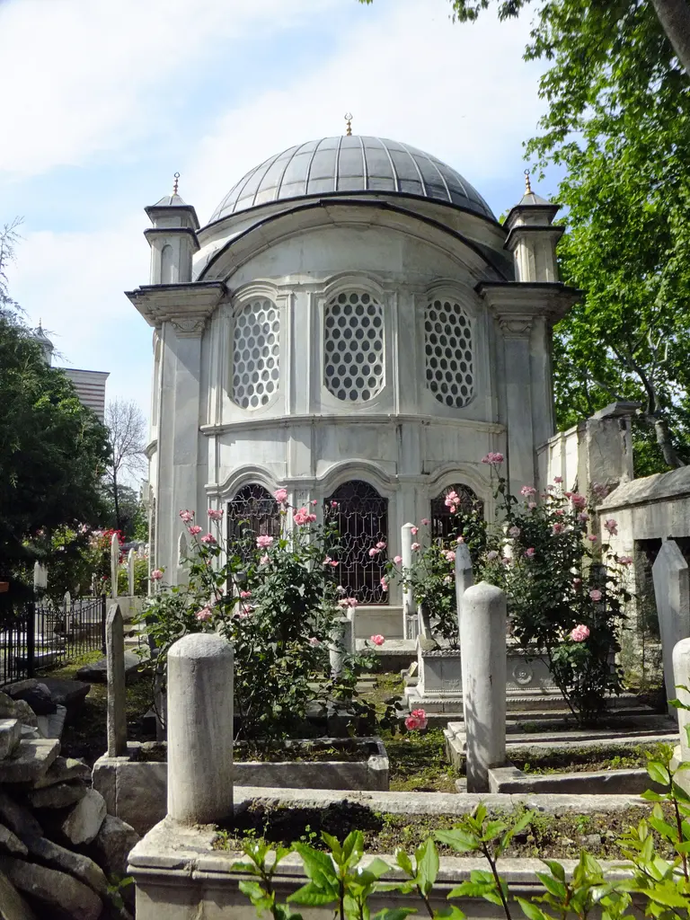 Şah Sultan Türbesi; mezar taşlarının ve açmış güllerin arasında mermer türbe, kubbe ve arkada ağaçlar.