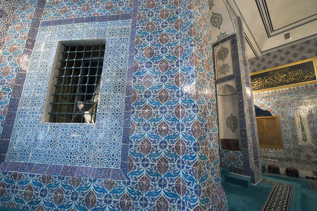 Eyüp Sultan Türbesi'nde çini kaplı duvar; mavi desenli paneller arasında demir parmaklıklı pencere ve yazı levhası.