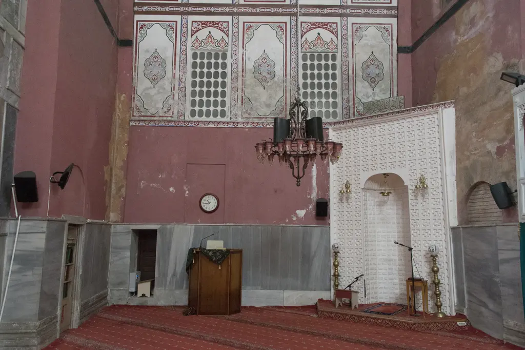 Kalenderhane Camii'nin mihrap duvarı; beyaz kafes desenli mihrap, pirinç şamdanlar, ahşap kürsü, avize ve üstte kalem işi panolar.