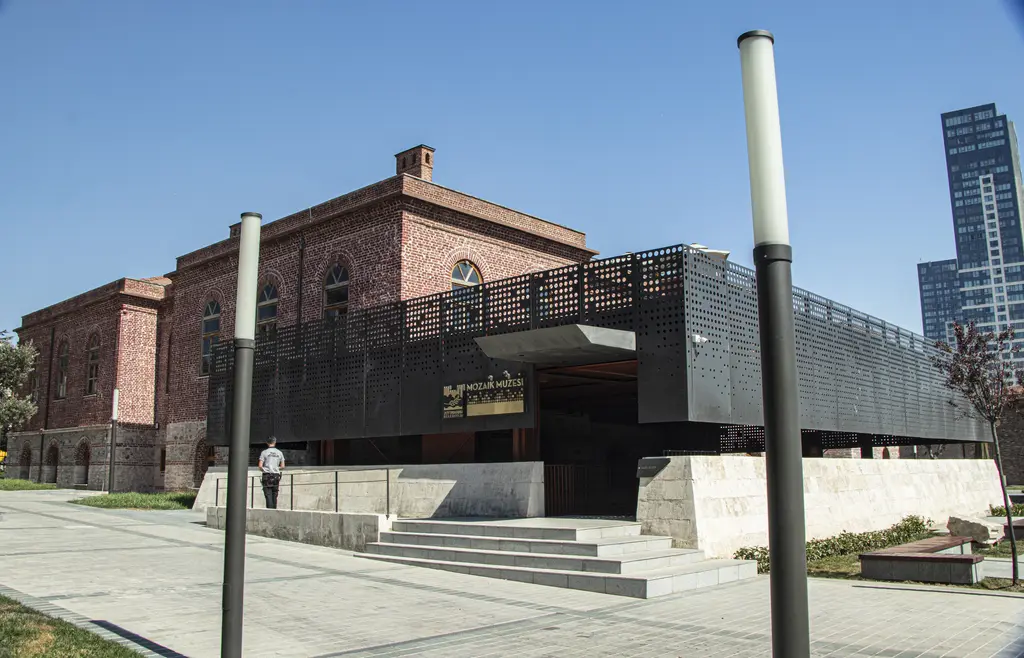 Kazlıçeşme Sanat'ın binası; solda tuğla cepheli tarihi yapı, sağda koyu renkli modern ek, önde geniş merdivenli meydan ve gökdelenler.