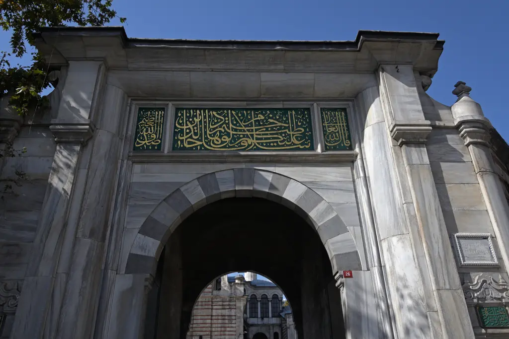 Laleli Camii'nin avlu kapısı; yuvarlak kemerli anıtsal açıklık, üstünde yeşil zeminli kitabe panosu ve iki yanda yivli pilastrlar.