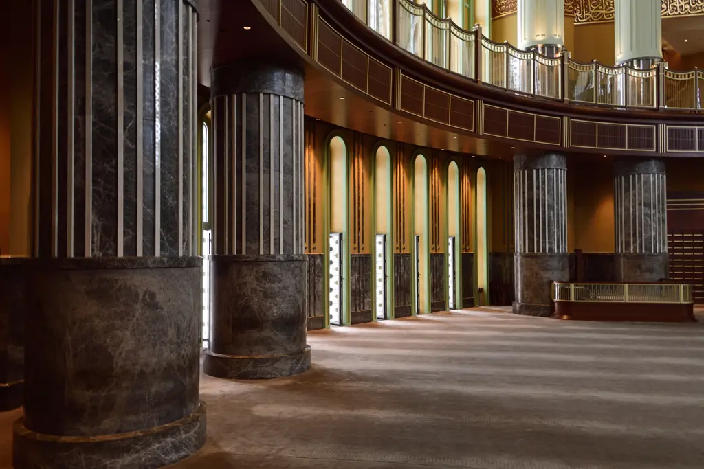 Taksim Camii'nde harimin kenarı; koyu mermer kaplı kalın sütunlar, üstte korkuluklu galeri ve duvar boyunca dar, uzun pencereler.