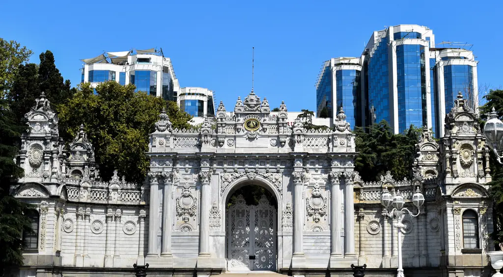 Dolmabahçe Sarayı'nın Saltanat Kapısı; karşıdan bakışta oymalı sütunlar, kemer, tepede tuğralı ve saatli süslü taç.