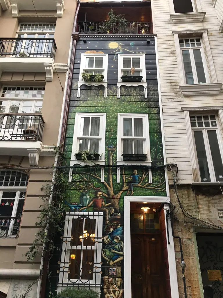 Çukurcuma'da dar, yeşil tonlu ve süslemelerle boyanmış bir apartman cephesi; iki yanda açık renkli binalar.