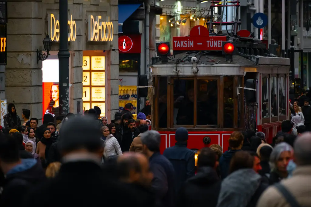 İstiklal Caddesi'nde yoğun kalabalık; ortada ilerleyen kırmızı tramvay, iki yanda mağaza tabelaları ve eski cepheler.