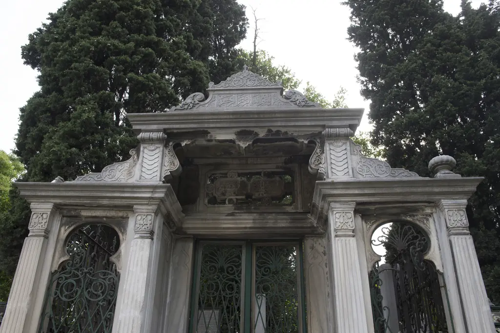 Eyüp Mezarlığı'nda hazire kapısı; ağaçlar arasında mermer sütunlu, alınlıklı giriş, demir şebekeli pencereler ve kemerler.