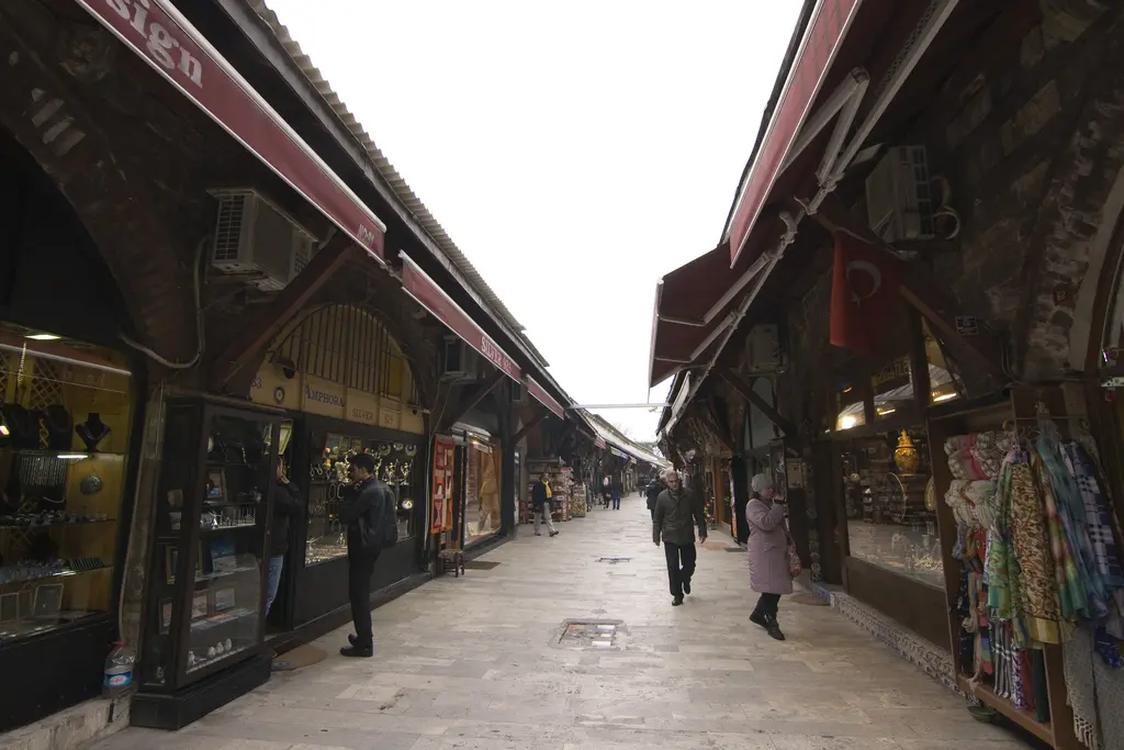 Arasta Çarşısı'nda tekstil dükkânları; asılı şallar ve giysiler, kemerli vitrinler, ahşap saçaklar ve sokağın sonuna uzanan sıra.