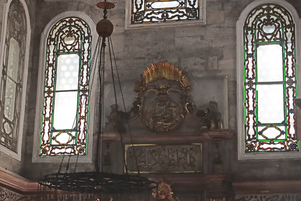 Eyüp Sultan Camii'nde mihrap duvarı; vitray pencereler, yaldızlı süslemeler, avize çemberi ve mermer mihrap.