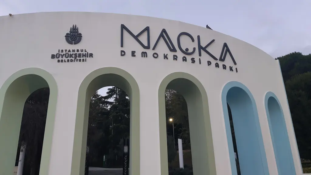 Maçka Demokrasi Parkı'nın beyaz kemerli giriş duvarı; açık mavi ve yeşil iç kemerler, üstte belediye logosu ve parkın adı.