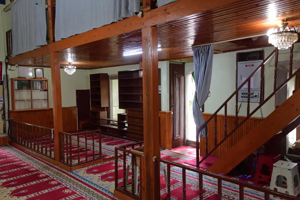 Defterdar Camii'nin ahşap mahfili; kahverengi direkler, mahfile çıkan merdiven, korkuluklar ve altında halı.