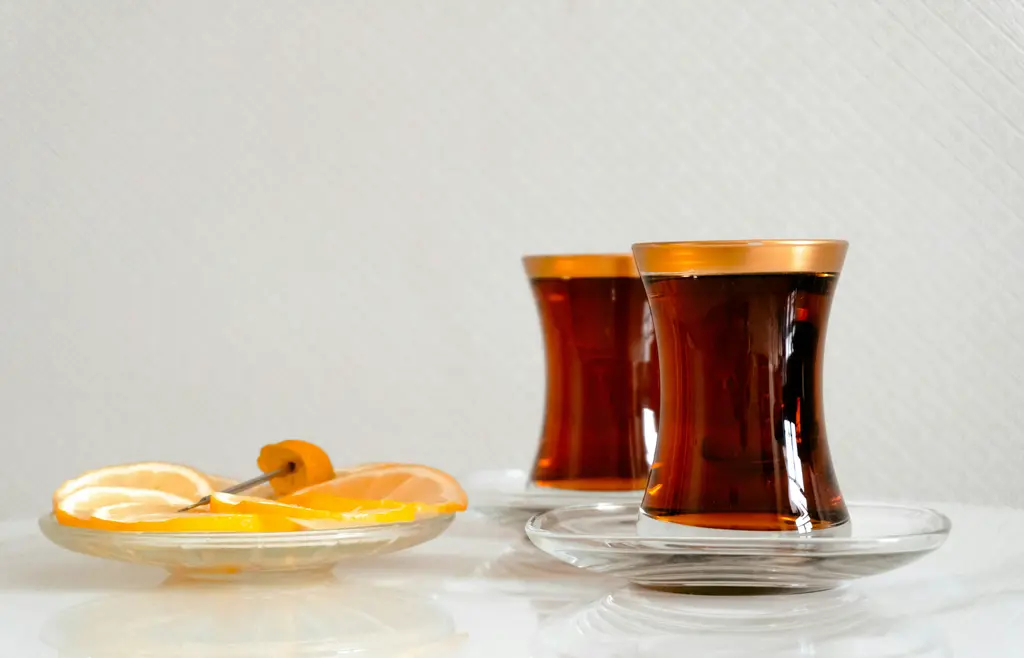 İnce belli armudu bardaklarda koyu demlenmiş çay; altın yaldızlı kenarlar, cam tabaklar ve yanında limon dilimleri.