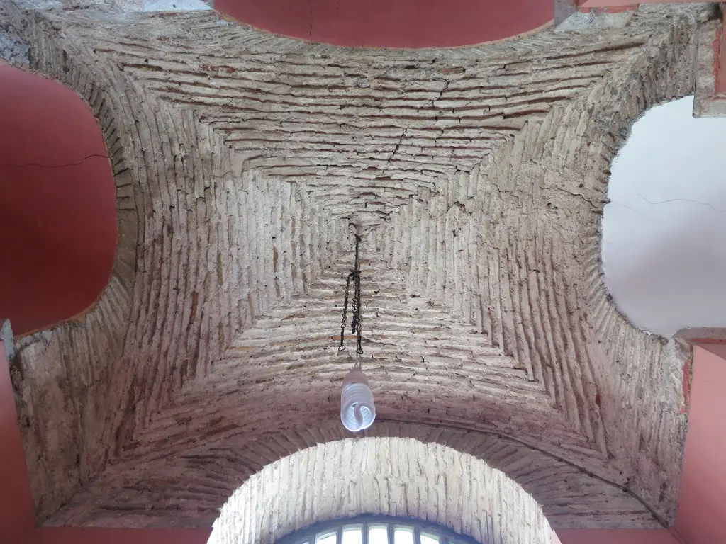 Kalenderhane Camii'nde çıplak tuğla çapraz tonoz; merkeze doğru daralan tuğla sıraları, zincire asılı lamba ve pembe kemer kavisleri.